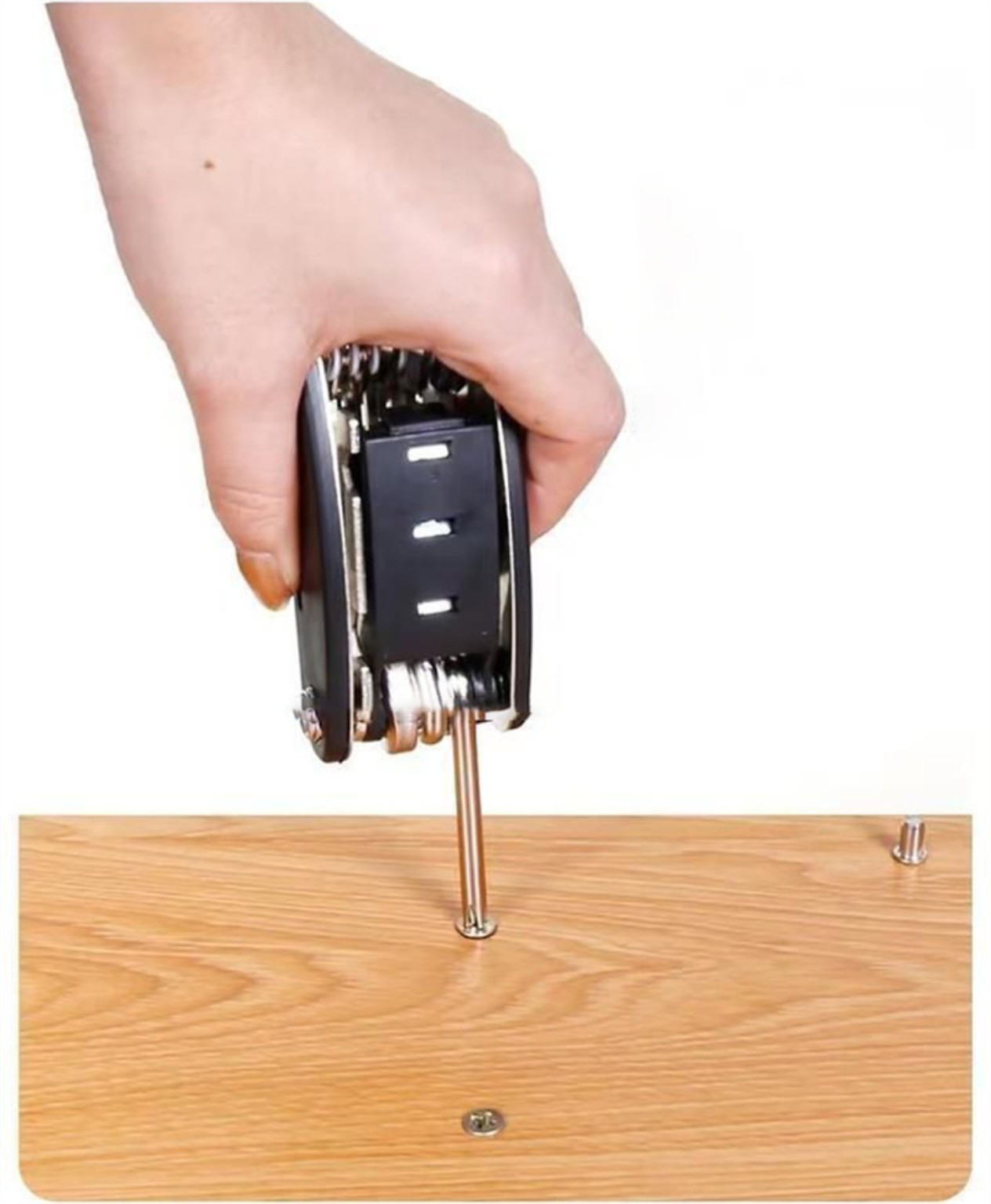 The multitool's extension bar and socket being used vertically on a small fastener in a wooden panel.